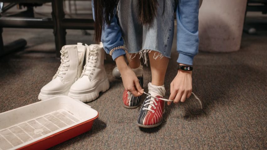 Close-up of a person tying bowling shoes, focused on footwear and hands indoors.